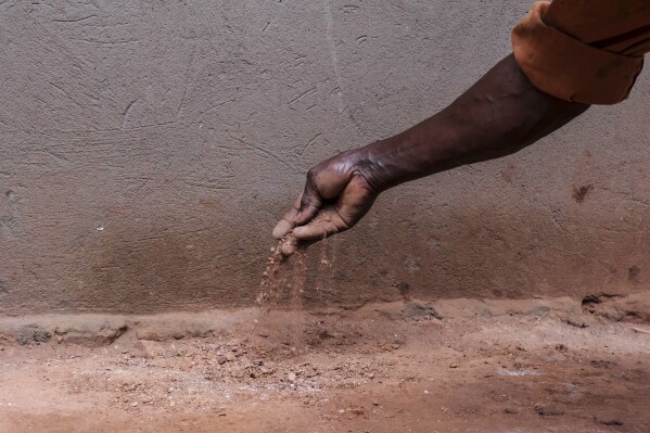 Simon Tigawalana shows dirt, that used to make up his home’s floor, before getting a clay-based earthen floor by a company called EarthEnable on May 16, 2025, in Jinja, Uganda. (AP Photo/Hajarah Nalwadda)