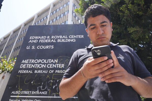 Alejandro Barranco checks his phone as he arrives to check on his father Narciso, who was detained by federal agents, outside the Metropolitan Detention Center on Monday, June 23, 2025, in Los Angeles. (AP Photo/Damian Dovarganes)