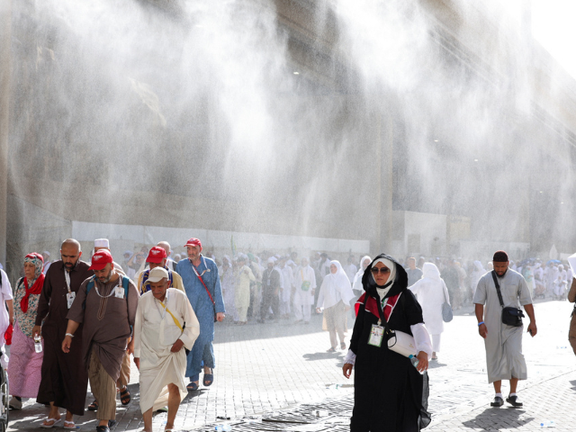 Muslim pilgrims walk as water sprinklers spray water during the annual hajj pilgrimage in Mina