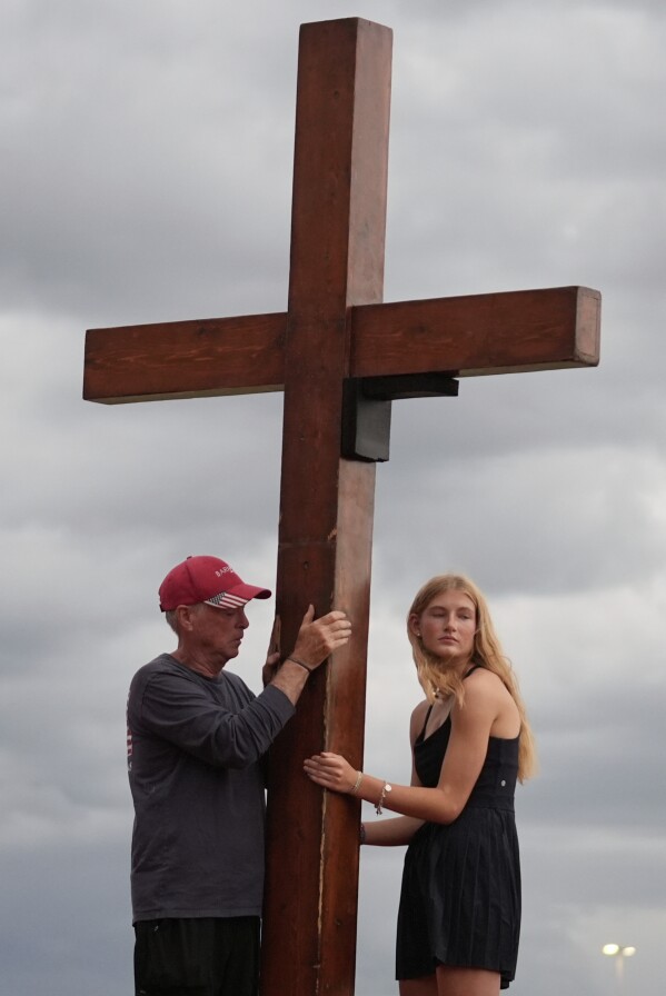 Dan Beazley, of Michigan, left, and Abigail Smithson hold a large cross during a vigil for flooding victims at Tivy Antler Stadium on Wednesday, July 9, 2025, in Kerrville, Texas. (AP Photo/Gerald Herbert)