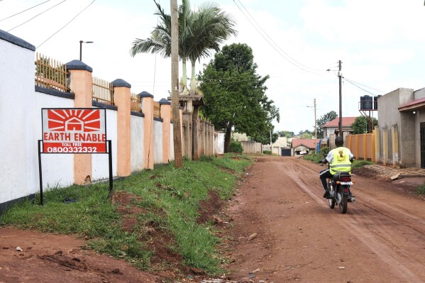 A person rides past a sign for EarthEnable on May 17, 2025, in Jinja, Uganda. (AP Photo/Hajarah Nalwadda)